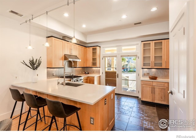 kitchen featuring visible vents, decorative backsplash, a breakfast bar area, and under cabinet range hood
