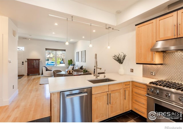 kitchen featuring a sink, a peninsula, under cabinet range hood, light brown cabinets, and stainless steel appliances