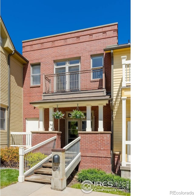 view of property featuring a porch, brick siding, and a balcony