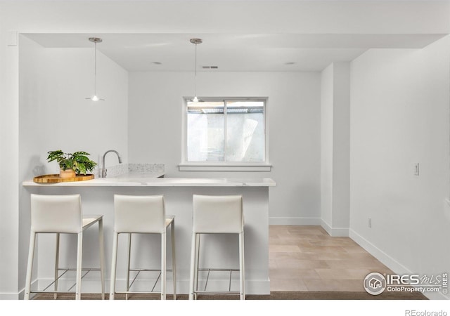 kitchen with baseboards, a breakfast bar, hanging light fixtures, and light countertops