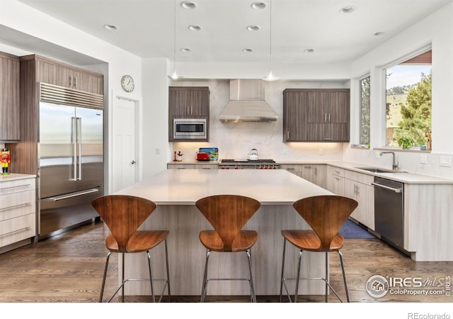 kitchen with built in appliances, dark wood-style floors, a breakfast bar area, and wall chimney exhaust hood