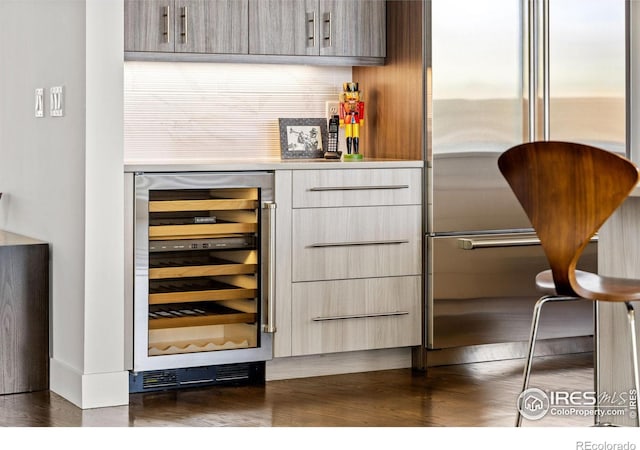 bar featuring stainless steel built in refrigerator, dark wood-style flooring, a dry bar, and beverage cooler