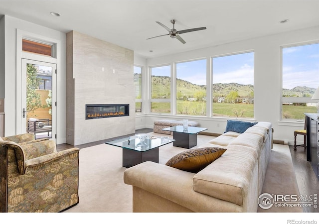 living area featuring a mountain view, wood finished floors, a ceiling fan, baseboards, and a tile fireplace