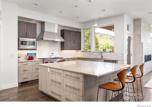 kitchen with stainless steel appliances, a kitchen breakfast bar, dark wood finished floors, modern cabinets, and wall chimney range hood