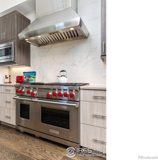 kitchen with wall chimney exhaust hood, dark wood-type flooring, backsplash, light countertops, and appliances with stainless steel finishes