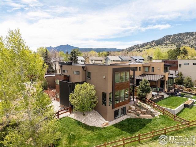 rear view of property featuring a mountain view, stucco siding, fence, and a lawn