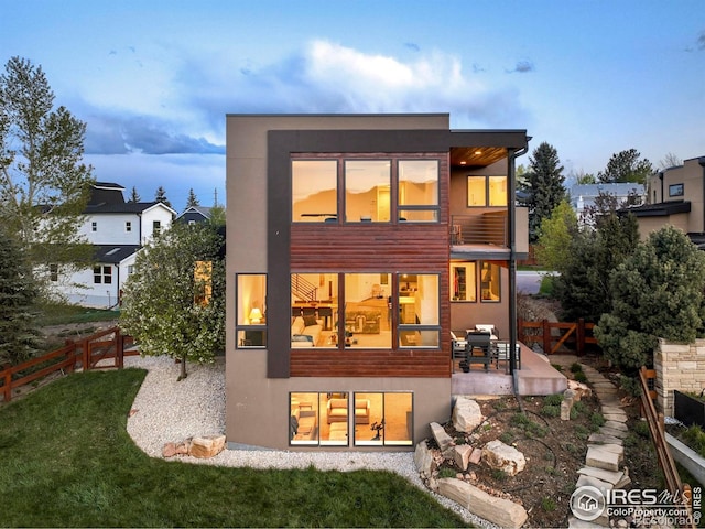 rear view of house with a lawn, a balcony, fence, a patio area, and stucco siding