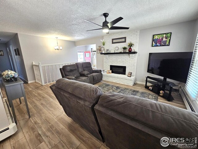 1628 Pheasant Rdg, Sterling, CO 80751 - living room with wood finished floors, a fireplace, a textured ceiling, a baseboard heating unit, and ceiling fan with notable chandelier