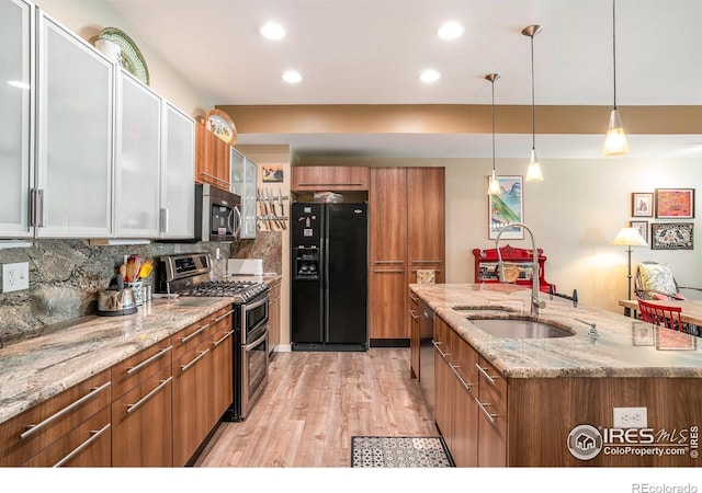 156 Brass Ct Unit 156, Loveland, CO 80537 - kitchen with brown cabinetry, stainless steel appliances, tasteful backsplash, a kitchen island with sink, and light wood-style flooring