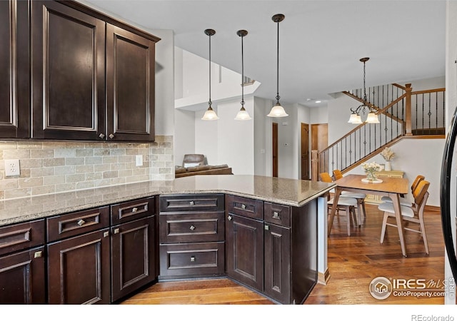 4822 Raven Run, Broomfield, CO 80023 - kitchen with a peninsula, dark brown cabinets, light wood-style floors, backsplash, and decorative light fixtures