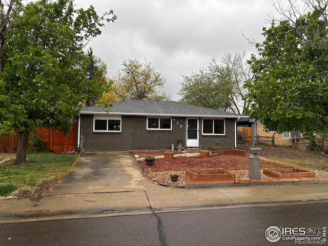 ranch-style home featuring brick siding, fence, a shingled roof, and driveway