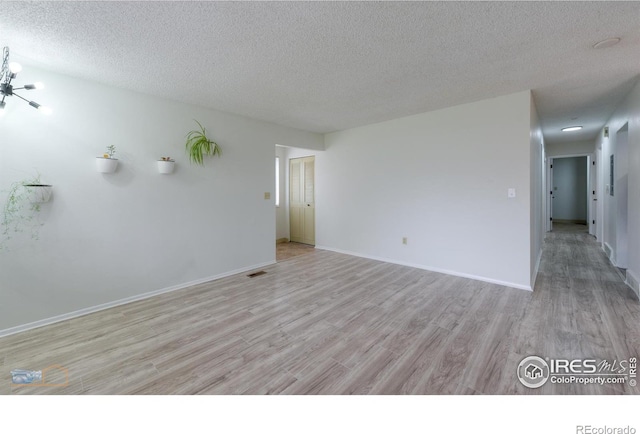spare room featuring a textured ceiling, baseboards, and light wood-type flooring