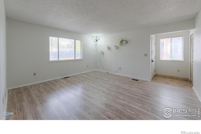 unfurnished room with light wood-type flooring, a textured ceiling, and visible vents