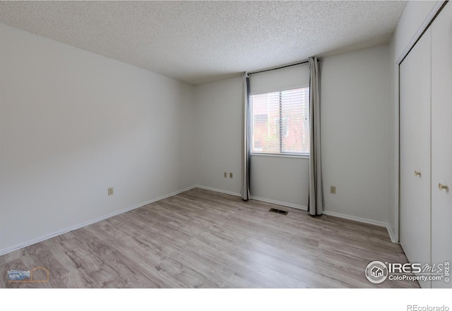 unfurnished bedroom with a textured ceiling, visible vents, light wood finished floors, and a closet