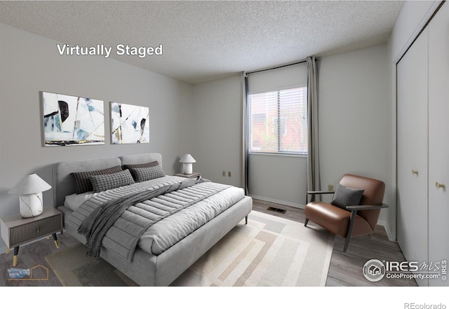 bedroom with a closet, visible vents, baseboards, a textured ceiling, and light wood finished floors