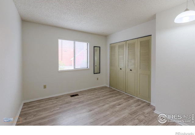 unfurnished bedroom featuring a textured ceiling, visible vents, light wood-type flooring, baseboards, and a closet
