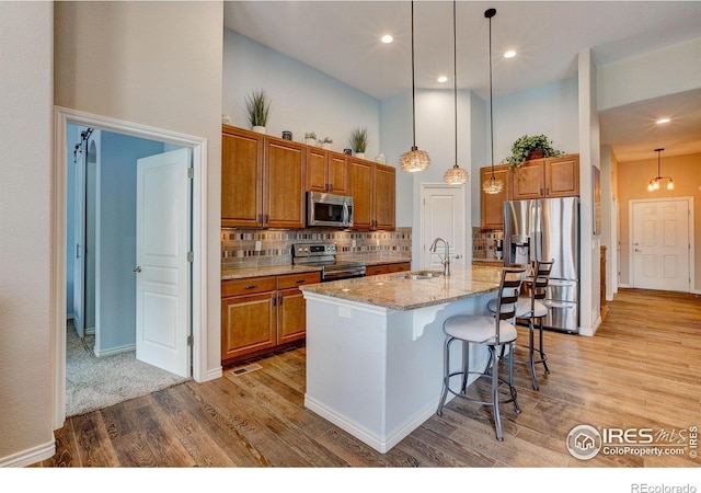 14394 W 88th Dr Unit C, Arvada, CO 80005 - kitchen with stainless steel appliances, a towering ceiling, brown cabinets, light wood-style floors, and light stone countertops