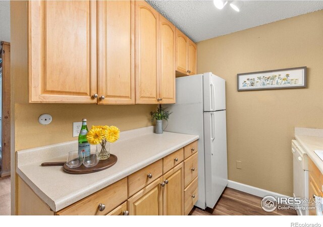 kitchen with light brown cabinets, light countertops, white appliances, baseboards, and wood finished floors