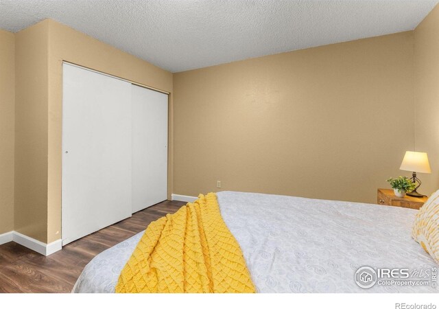 bedroom with a closet, a textured ceiling, baseboards, and wood finished floors