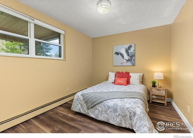 bedroom featuring a textured ceiling, baseboards, baseboard heating, and wood finished floors