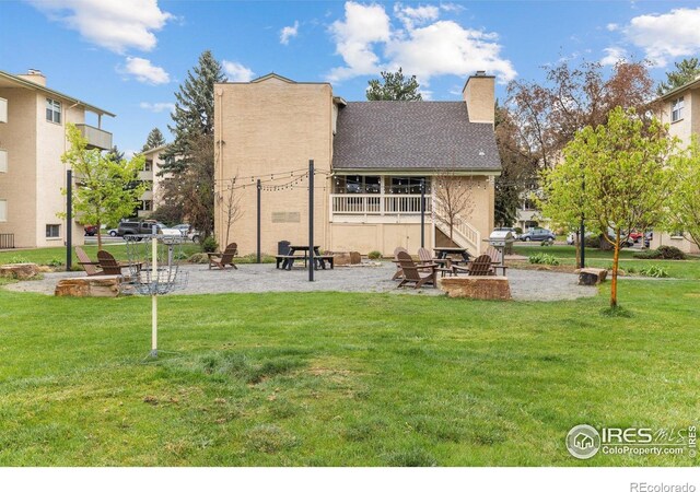 rear view of house with a lawn, a patio, a chimney, and roof with shingles