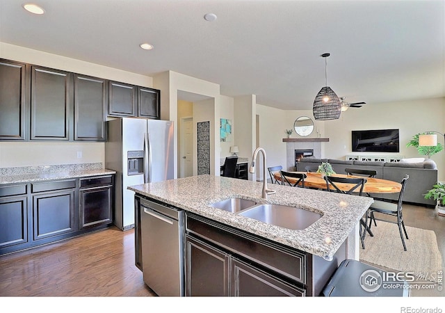 2927 Percheron Dr, Fort Collins, CO 80525 - kitchen featuring a fireplace, open floor plan, light stone counters, a sink, and stainless steel appliances