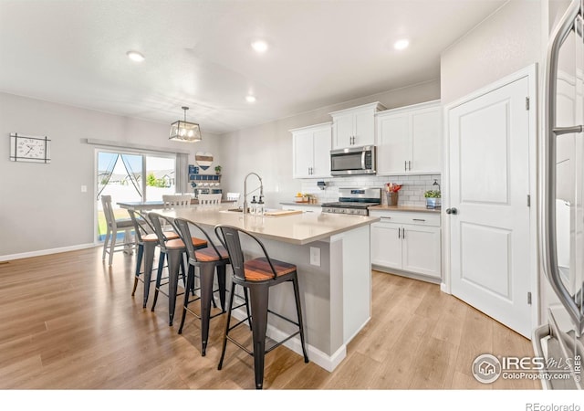 kitchen featuring appliances with stainless steel finishes, a breakfast bar, a sink, light wood-style flooring, and tasteful backsplash