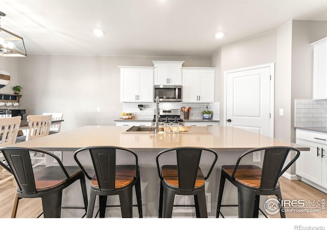 kitchen featuring a kitchen island with sink, backsplash, appliances with stainless steel finishes, light wood-type flooring, and white cabinetry