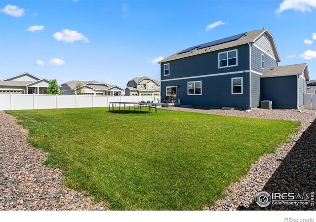 rear view of property with a trampoline, a residential view, a fenced backyard, roof mounted solar panels, and a yard