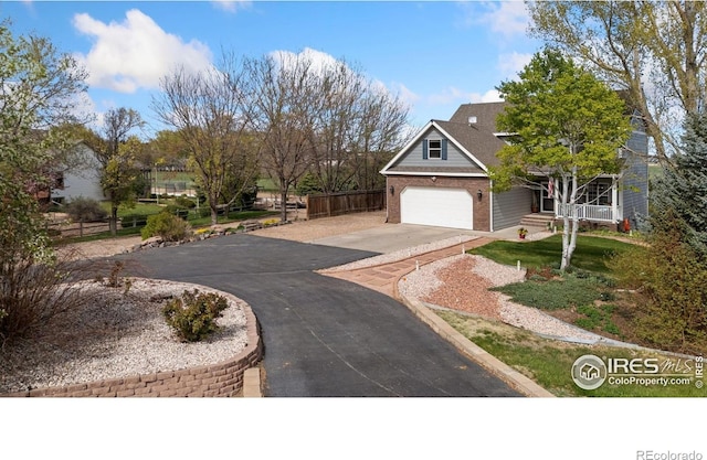 view of front facade featuring brick siding, an attached garage, fence, and aphalt driveway
