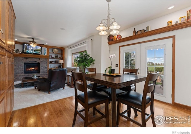 dining space featuring a brick fireplace, ceiling fan with notable chandelier, light wood-type flooring, and plenty of natural light