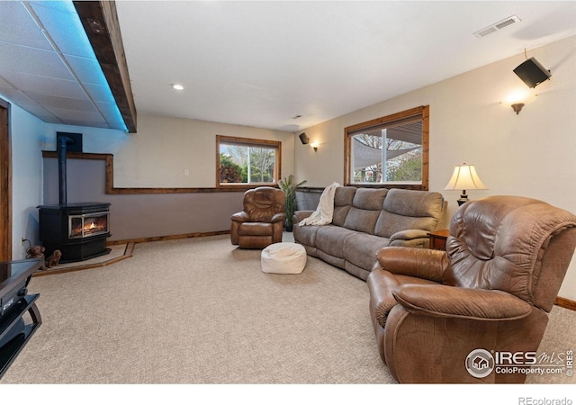 carpeted living area featuring a wood stove, visible vents, baseboards, and recessed lighting