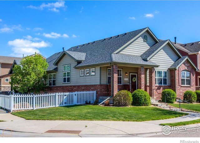 view of front of home with brick siding, a front lawn, roof with shingles, and fence