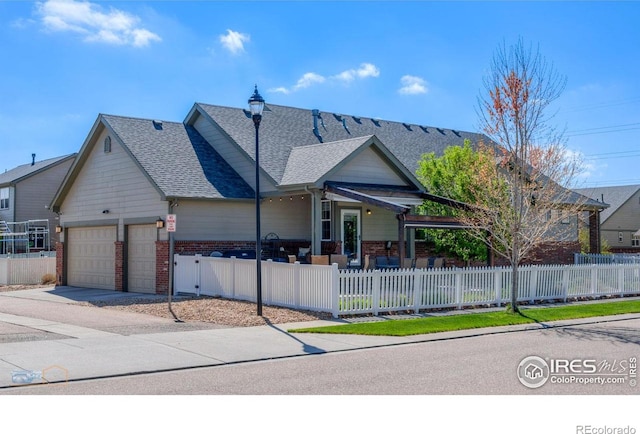 view of front facade featuring roof with shingles, brick siding, concrete driveway, an attached garage, and a fenced front yard