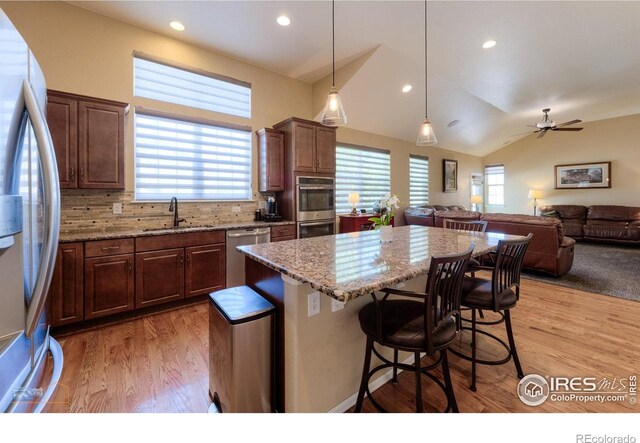 kitchen with a kitchen island, light stone countertops, a sink, light wood finished floors, and stainless steel appliances