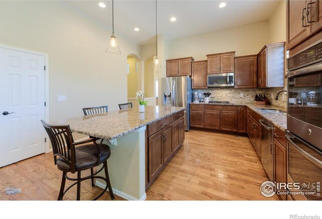kitchen with a sink, a kitchen breakfast bar, arched walkways, light wood finished floors, and appliances with stainless steel finishes