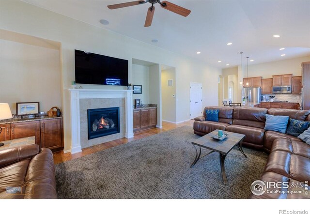 living area featuring ceiling fan, a tile fireplace, baseboards, light wood-style floors, and recessed lighting