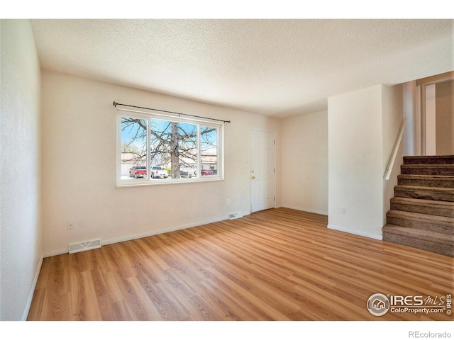 empty room with stairway, baseboards, wood finished floors, and visible vents