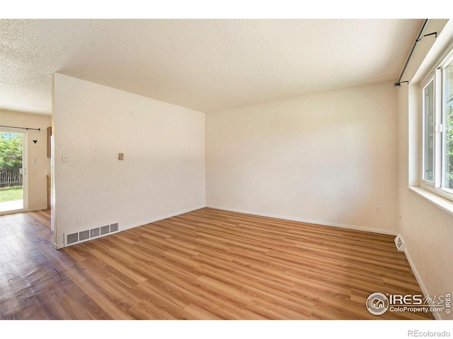 empty room with visible vents, a textured ceiling, light wood finished floors, and baseboards