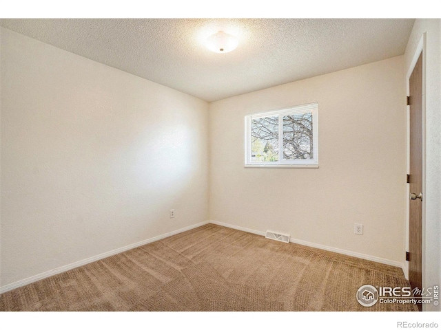 spare room featuring carpet flooring, a textured ceiling, baseboards, and visible vents