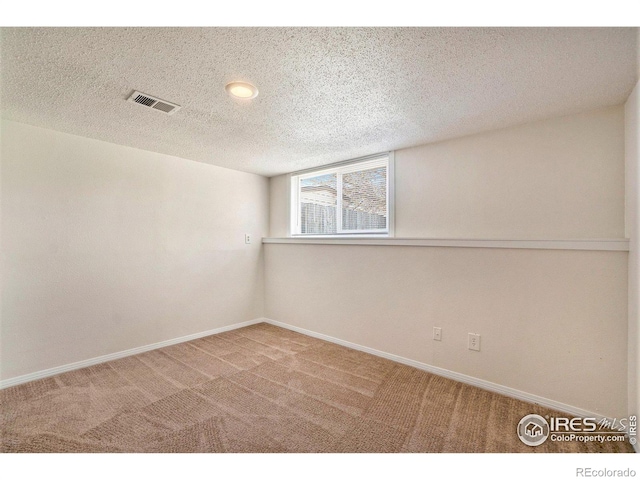 empty room with carpet floors, a textured ceiling, baseboards, and visible vents