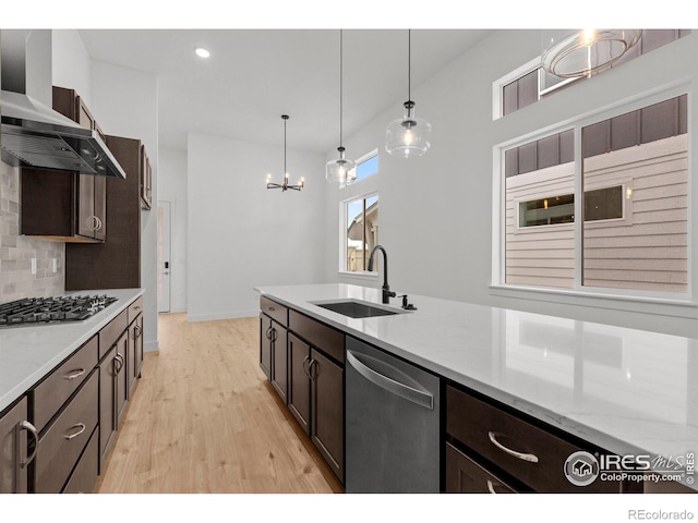 kitchen featuring dark brown cabinets, light wood-style floors, wall chimney range hood, a sink, and stainless steel appliances