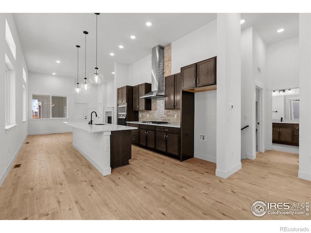 kitchen with wall chimney range hood, dark brown cabinets, a sink, light countertops, and tasteful backsplash