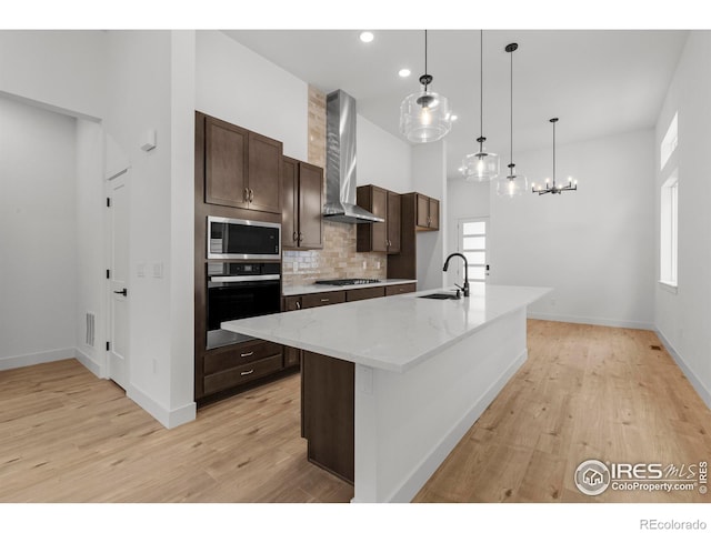kitchen featuring a sink, light wood-style flooring, stainless steel appliances, and wall chimney exhaust hood