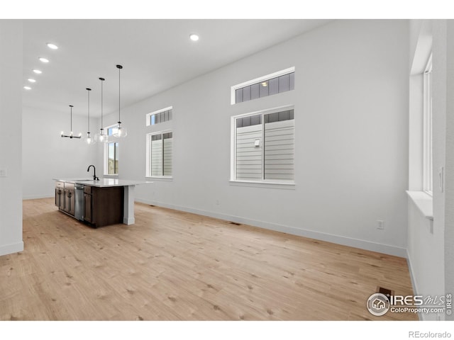 kitchen with stainless steel dishwasher, a center island with sink, a sink, and light wood-style flooring