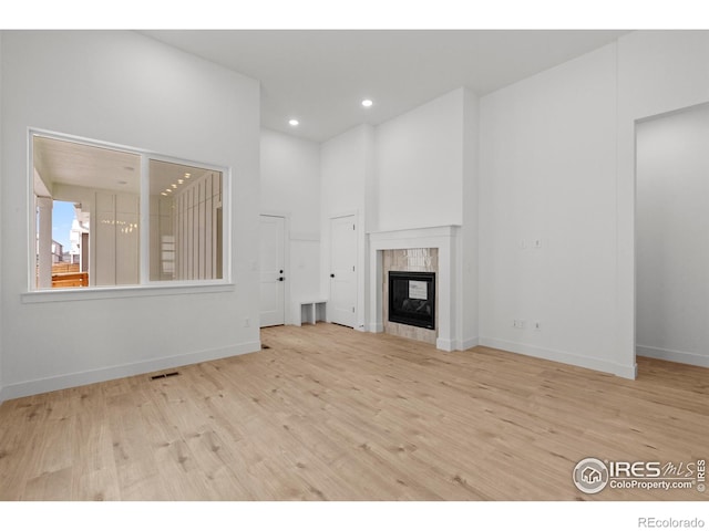 unfurnished living room featuring a high end fireplace, baseboards, wood finished floors, and visible vents