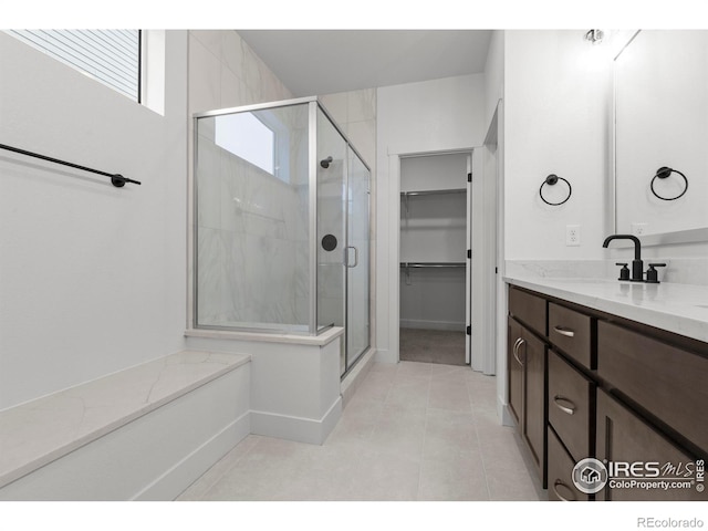 bathroom featuring a walk in closet, a stall shower, vanity, baseboards, and tile patterned floors