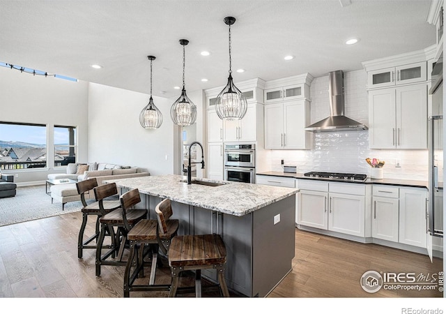 3295 Heron Lakes Pkwy, Berthoud, CO 80513 - kitchen with wall chimney range hood, backsplash, a sink, stainless steel appliances, and an island with sink