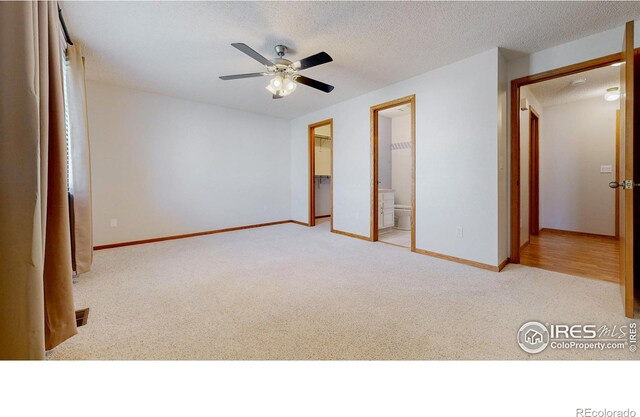 unfurnished bedroom with carpet flooring, ensuite bath, a ceiling fan, baseboards, and a spacious closet