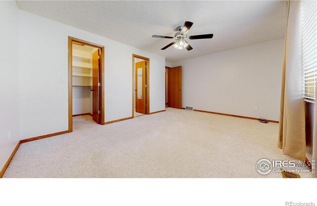 interior space with ceiling fan, light colored carpet, a walk in closet, baseboards, and a closet